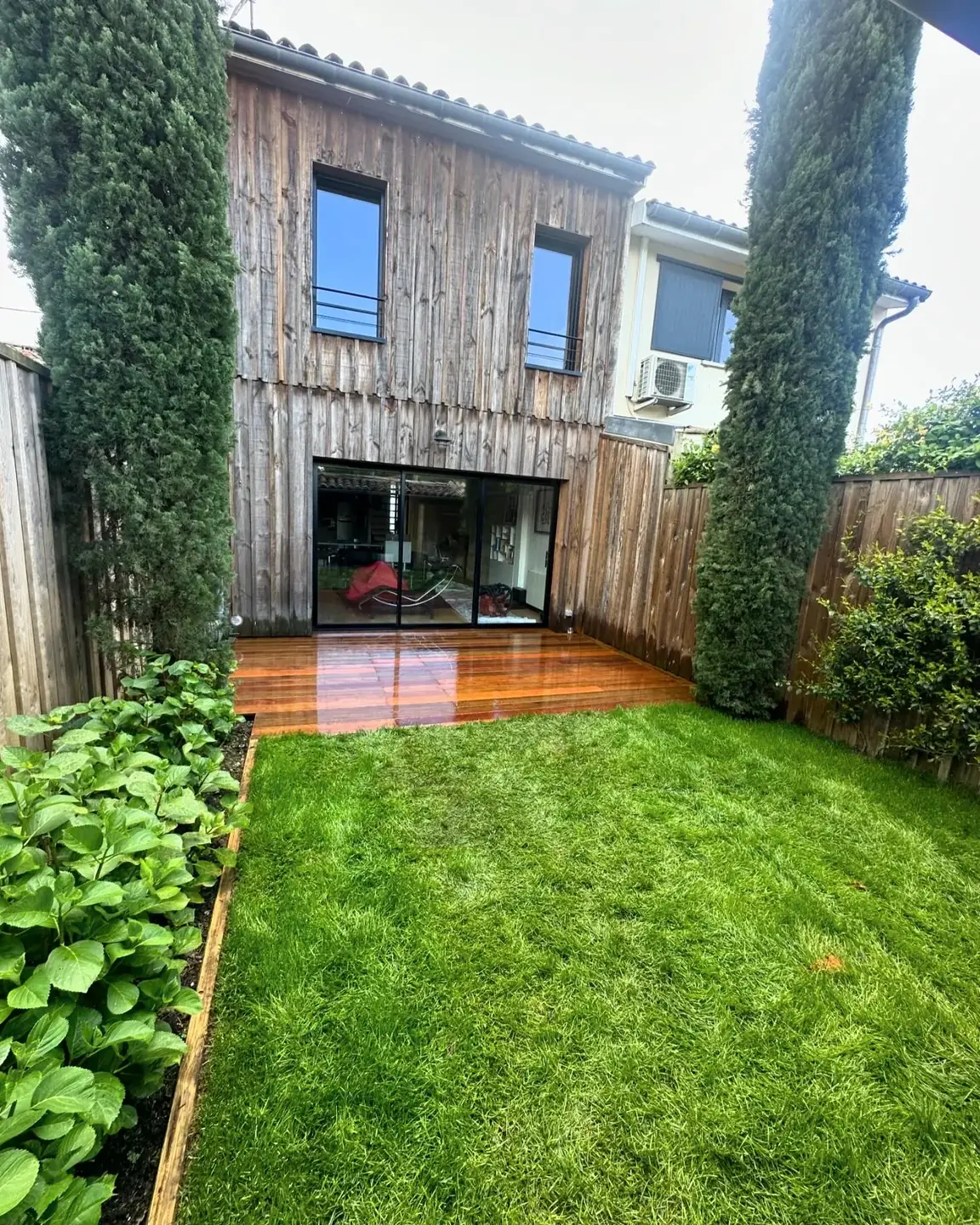 Terrasse en bois devant une maison bardée de bois et un jardin vert
